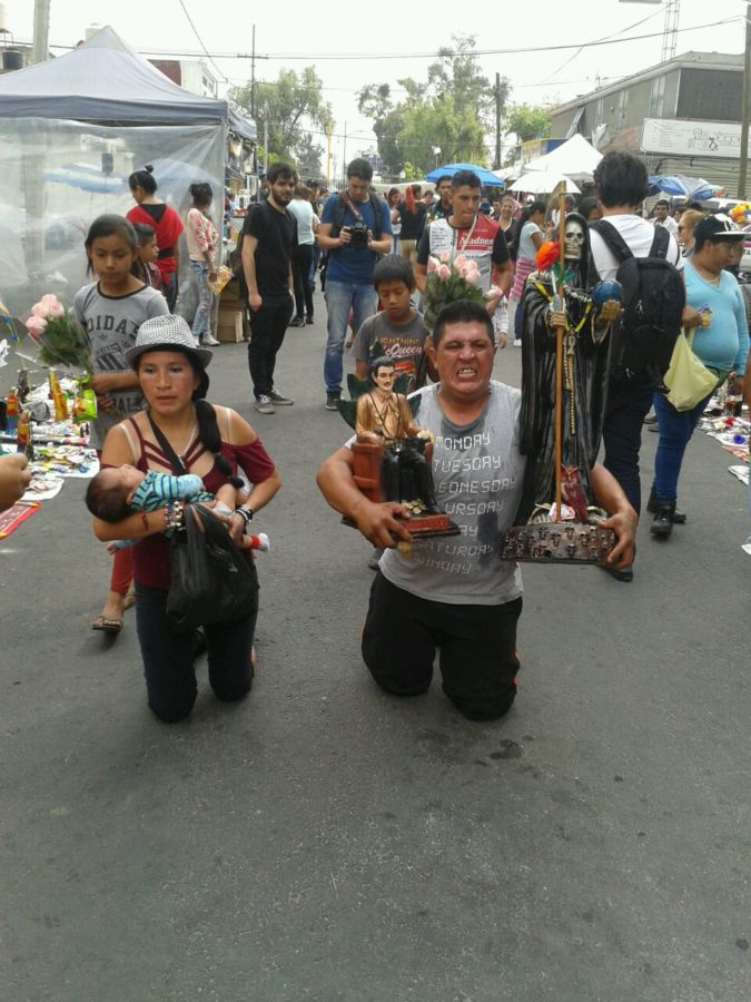 Devotees on their knees to reach Doña Enriqueta Romero’s public altar. The man is holding the figure of the Santa Muerte in his left hand and one of Jesús Malverde in his right. Malverde is another folk saint associated with drug trafficking but also a type of Robin Hood figure who stole from the rich to give to the poor. Alfarería Street, Tepito, Mexico City, April 1, 2019. Photo: Jessie Marroquín.